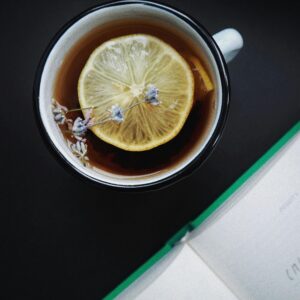 A close-up view of a lemon herbal tea with lavender flowers and an open book in the background. Perfect cozy moment indoors.