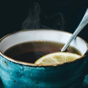 Close-up of aromatic steaming lemon herbal tea served in a ceramic cup with saucer.